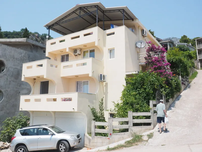 Dreistöckiges Haus in Bar, Montenegro: helle Fassade, Terrassen, Garage und blühende Bougainvillea auf dem Grundstück.