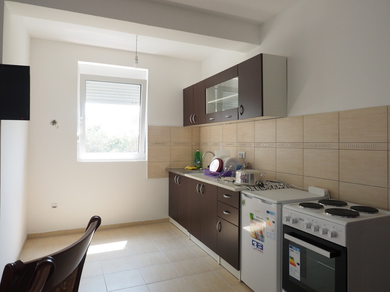 Küche in einer Wohnung in Šušanj, Montenegro: dunkle Einbauküche, weißer Herd, Kühlschrank und helle Fliesenverkleidung.