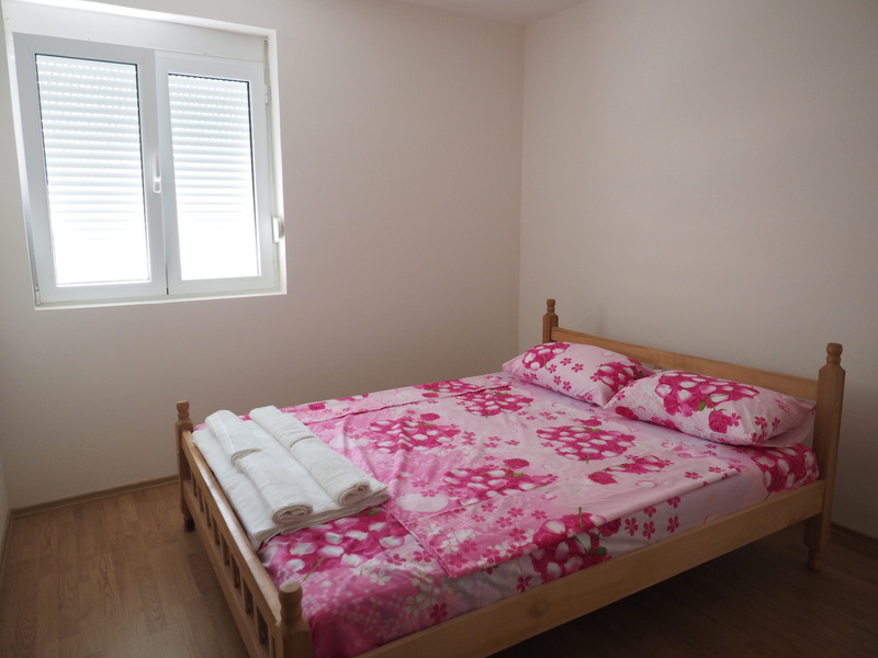 Helles Schlafzimmer mit Doppelbett in einer Wohnung in Šušanj, Montenegro: Holzmöbel und Kunststofffenster.