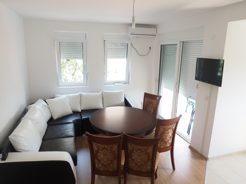 Wohnzimmer in einer Wohnung in Šušanj, Montenegro: Ecksofa, Essbereich mit rundem Tisch und Ausgang zur Terrasse.