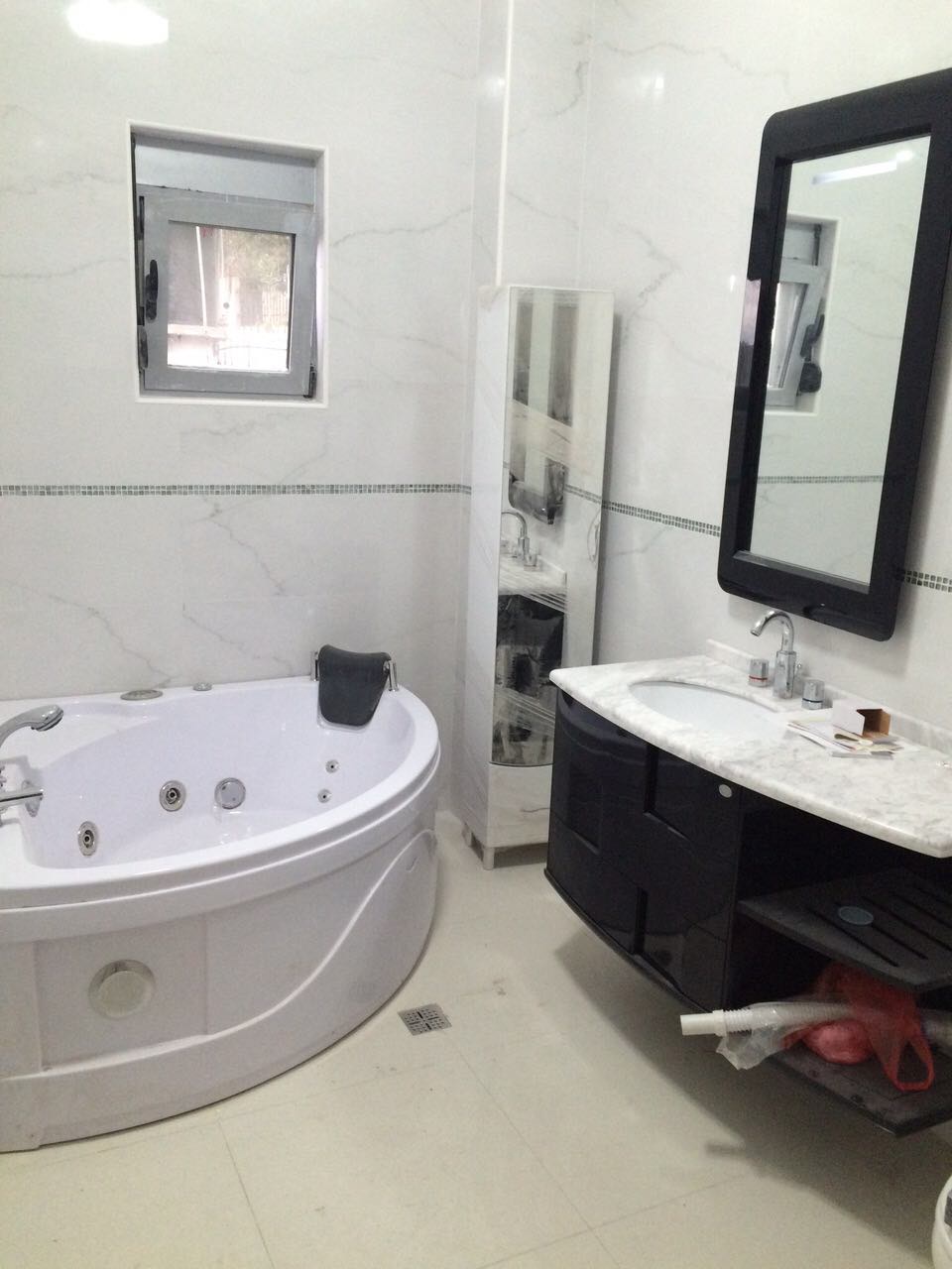 Badezimmer mit Whirlpool und schwarzen Möbeln im Haus, Šušanj, Montenegro. Helle Fliesen in Marmoroptik, modernes Interieur.