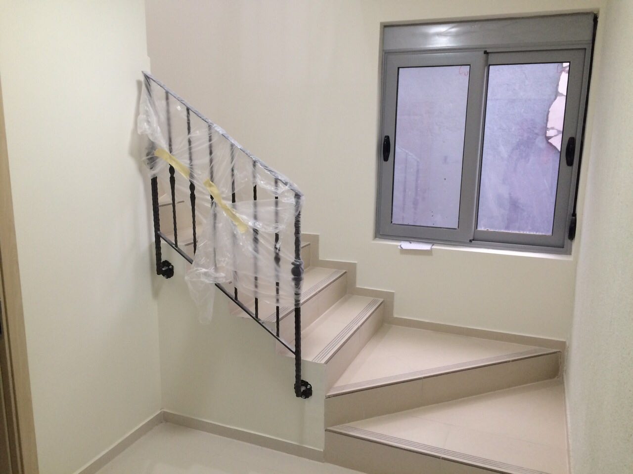 Treppe mit schmiedeeisernem Geländer und hellen Fliesen in einem Neubau in Šušanj, Montenegro. Innenausbau, Blick auf das Fenster.
