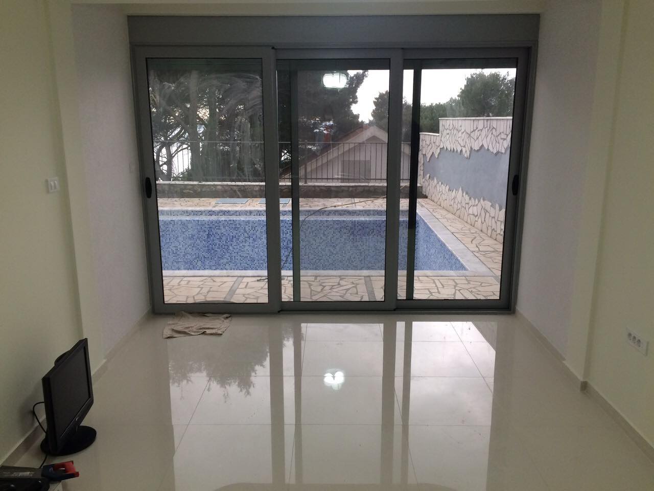 Wohnzimmer mit Panoramafenster und Zugang zum Pool im Haus, Shushan, Montenegro. Helles Interieur mit glänzendem Boden.