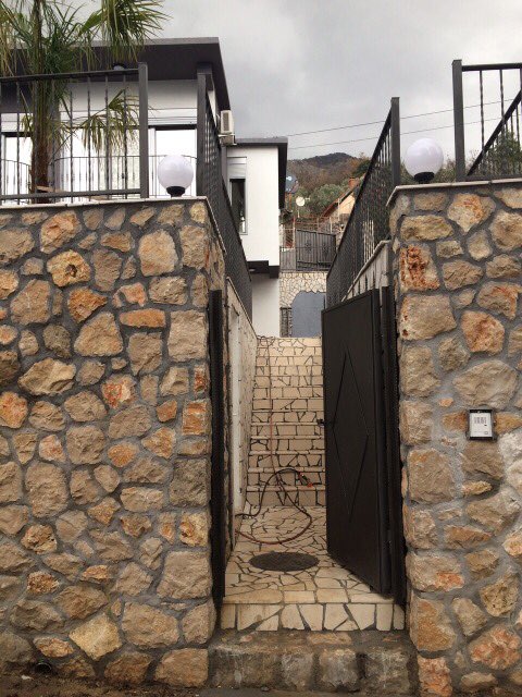Eingang zum Haus in Šušanj, Montenegro: Fassadenverkleidung aus Stein, Treppe aus Naturstein und modernes Tor.