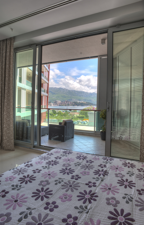 Schlafzimmer in einer Wohnung in Budva, Montenegro, mit Panoramablick auf das Meer und die Berge sowie Zugang zu einer möblierten Terrasse.