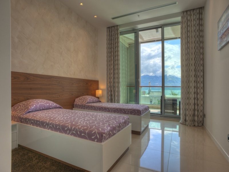 Schlafzimmer in einer Wohnung in Budva, Montenegro: zwei Betten, Panoramafenster mit Blick auf das Meer und die Berge, moderne Ausstattung.