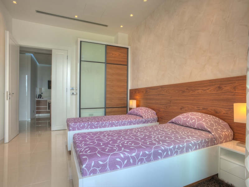 Modernes Schlafzimmer mit zwei Betten in einer Wohnung in Budva, Montenegro: Einbauschrank, helle Ausstattung und Fliesen.
