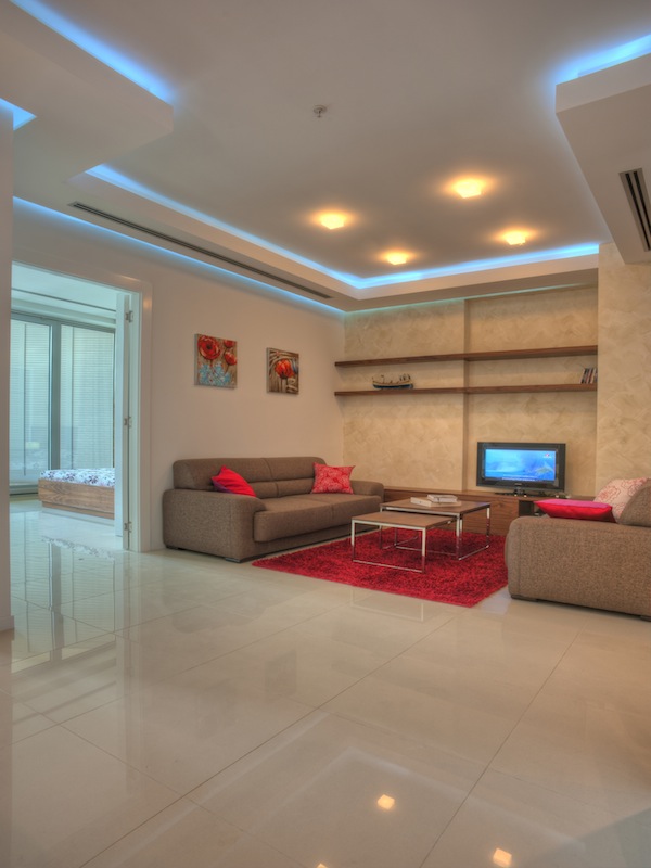 Modernes Wohnzimmer in einer Wohnung in Budva, Montenegro: beige Möbel, roter Teppich, Deckenbeleuchtung und Fliesen.