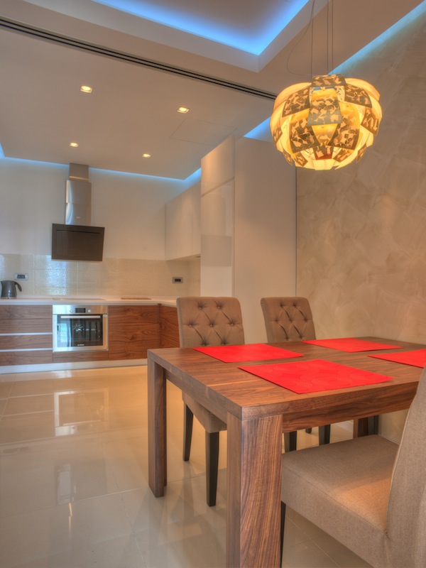 Moderne Wohnküche in einer Wohnung in Budva, Montenegro: Holz-Einbauküche, Essbereich und Designerbeleuchtung.