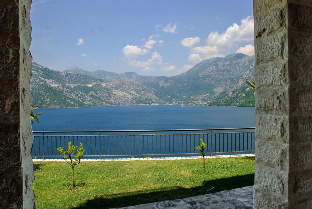 Vue sur la baie de Kotor et les montagnes depuis la terrasse de l’appartement à Kostanica, Monténégro : colonnes en pierre et pelouse verte.
