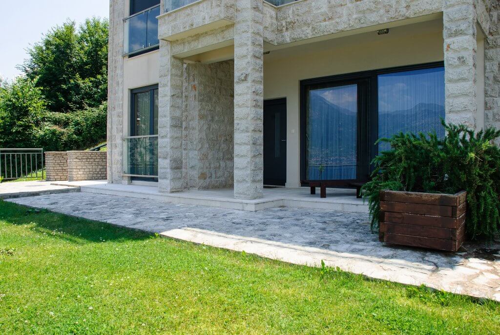 Terrasse de l’appartement à Kostanica, Monténégro : façade en pierre, baies vitrées panoramiques et vue sur les montagnes et la mer.