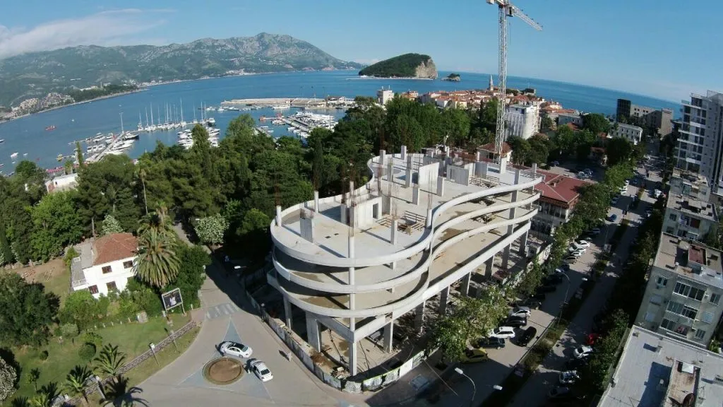 Im Bau befindliche Wohnanlage in Budva, Montenegro: Luftaufnahme eines Massivgebäudes am Meer und des Yachthafens.