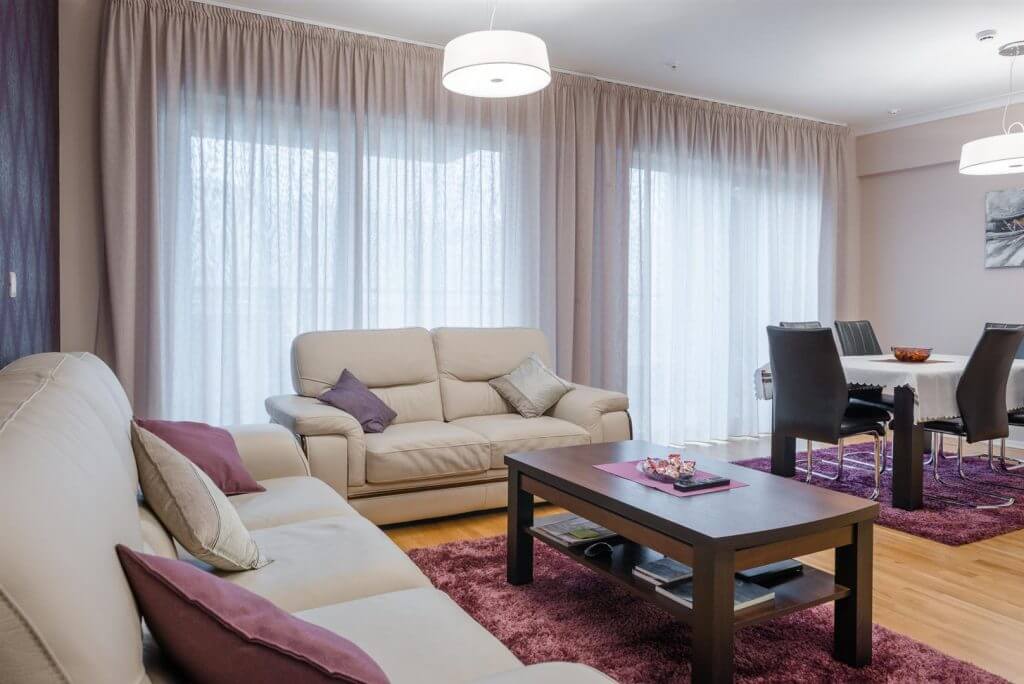 Svetao dnevni boravak sa kožnim sofama i trpezarijskim delom u stanu u Bečićima, Crna Gora. Moderan enterijer.