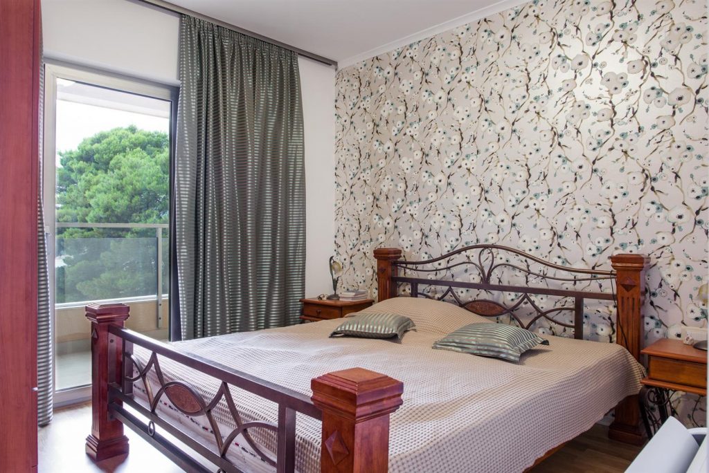Spavaća soba sa bračnim krevetom, tapetama sa cvetnim printom i izlazom na balkon u stanu, Bečići, Crna Gora.