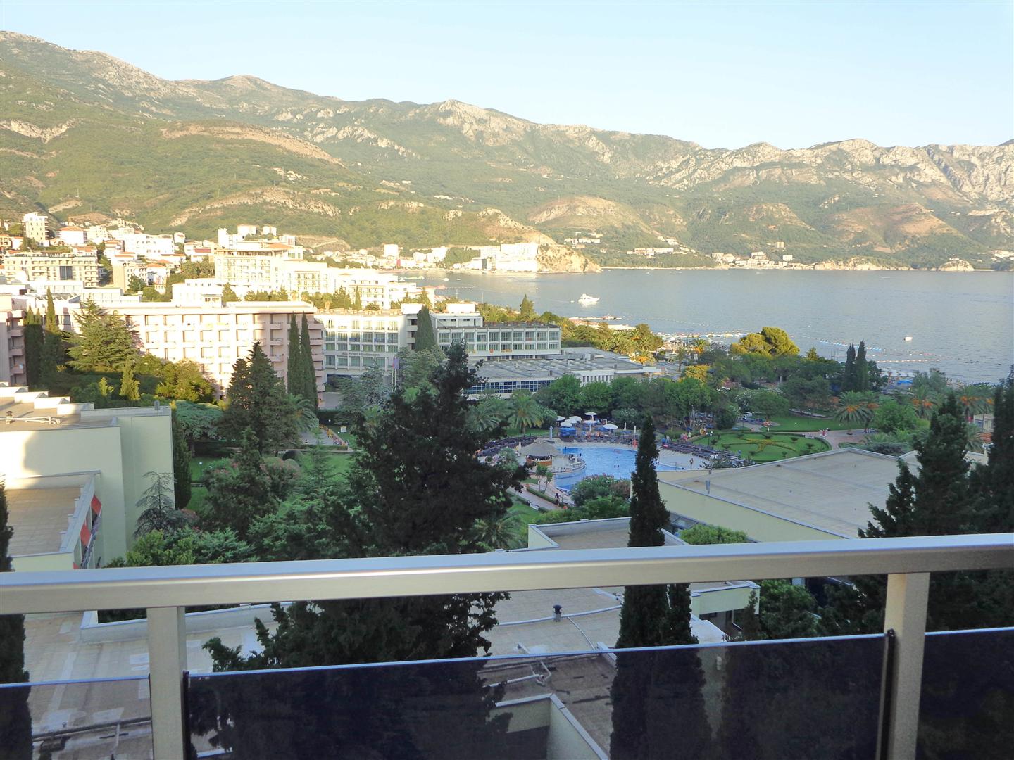 Pogled s balkona na more, planine i letovalište Bečići u Crnoj Gori, panorama obale sa hotelima i bazenom.