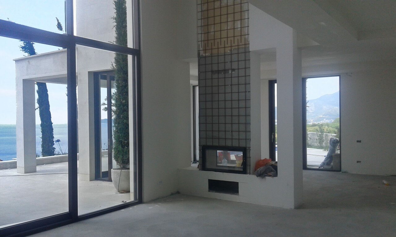 Wohnzimmer in einer Villa in Reževići, Montenegro: Panoramafenster, Meerblick, Kamin in der Fertigstellung und Terrasse.