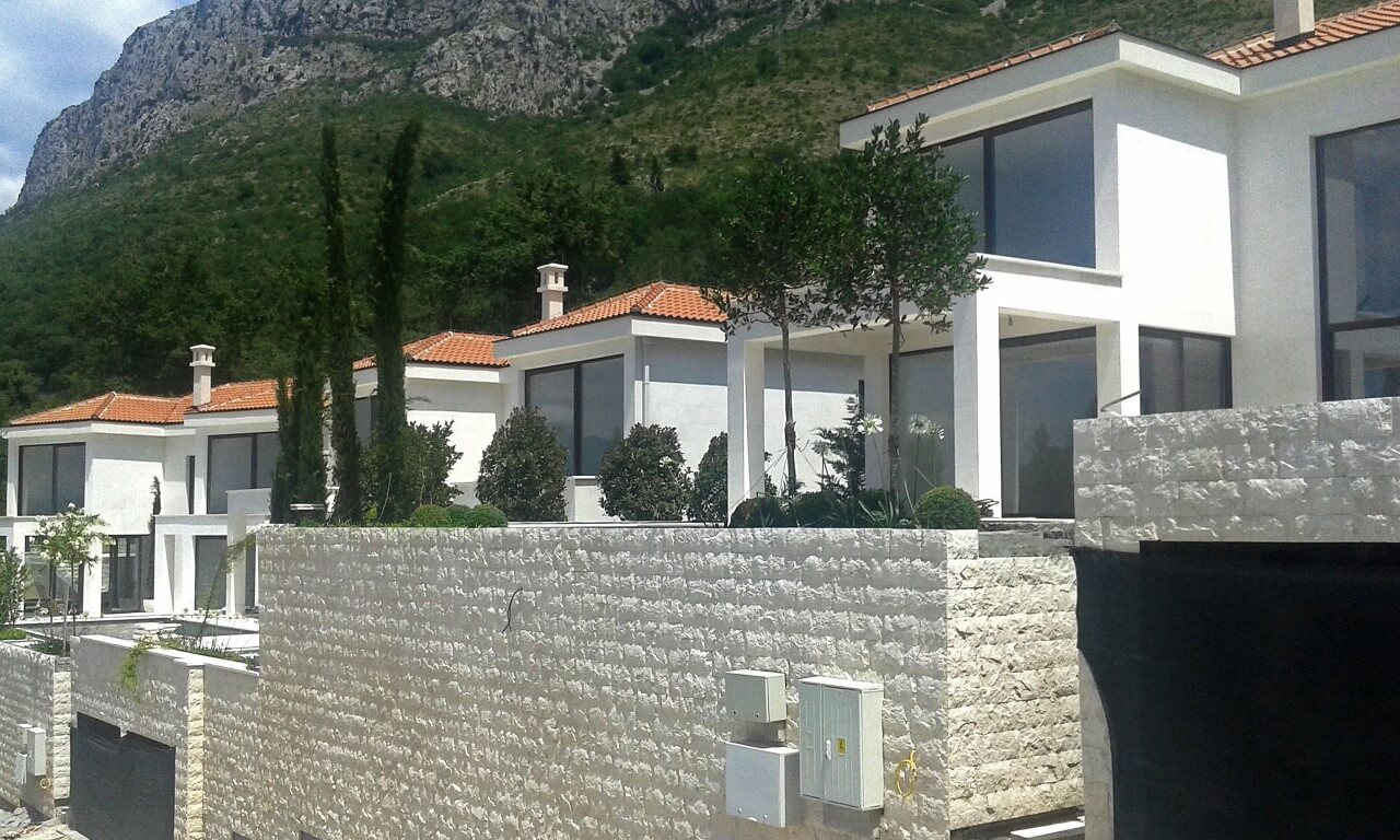 Moderne Villen mit Panoramafenstern und Steinverkleidung in Reževići, Montenegro, vor Bergkulisse.