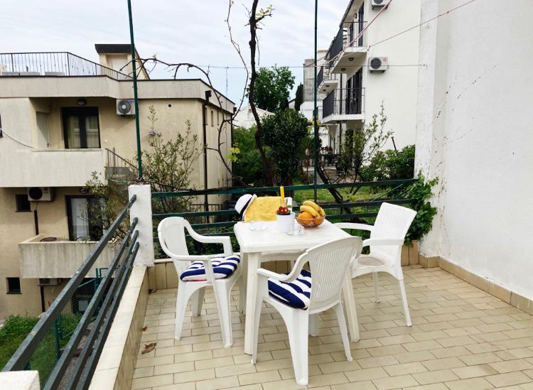 Gemütliche Terrasse mit Kunststoffmöbeln und Blick auf die Stadt im Hotel in Budva, Montenegro. Balkon mit Fliesen und Grünpflanzen.