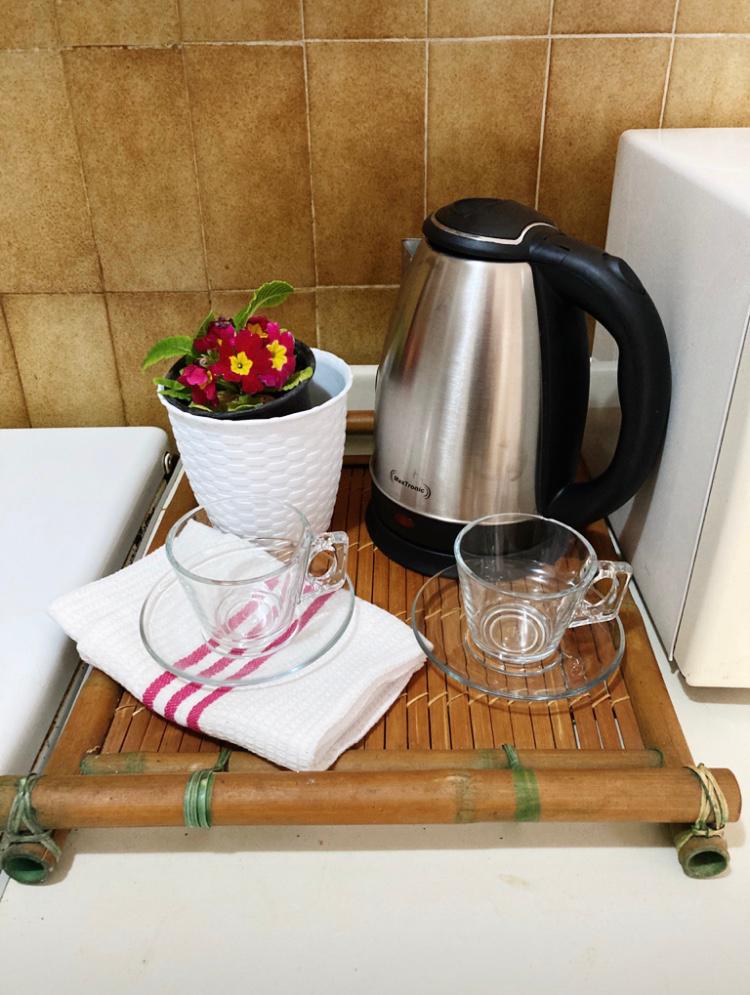 Küchenecke im Hotel in Budva, Montenegro: Wasserkocher, Glasbecher auf einem Bambustablett und Blumendekor.
