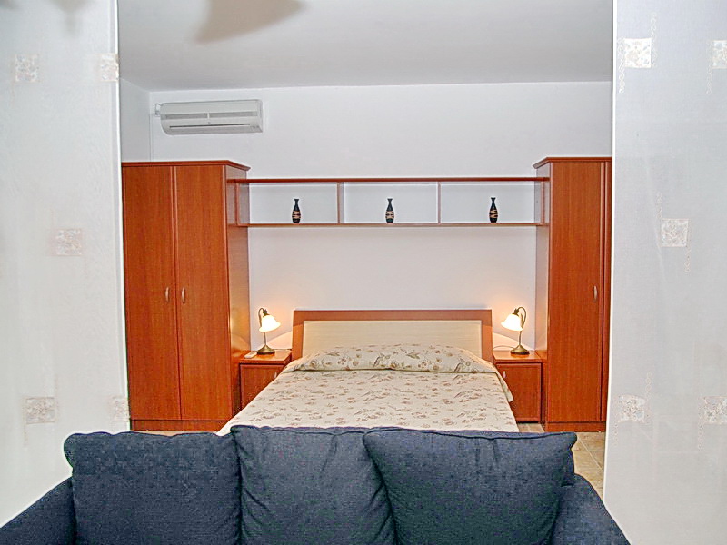 Schlafzimmer in einem Hotel in Budva, Montenegro: Doppelbett, Holzmöbel, Nachttischlampen und Klimaanlage.