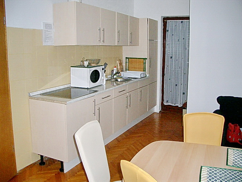 Küche im Hotel in Budva, Montenegro: helle Einbauküche, Essbereich, Parkettboden und Zugang zum Balkon.