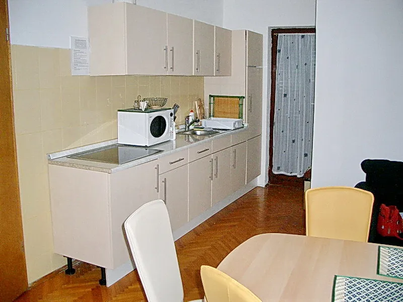 Küche im Hotel in Budva, Montenegro: helle Einbauküche, Essbereich, Parkettboden und Zugang zum Balkon.