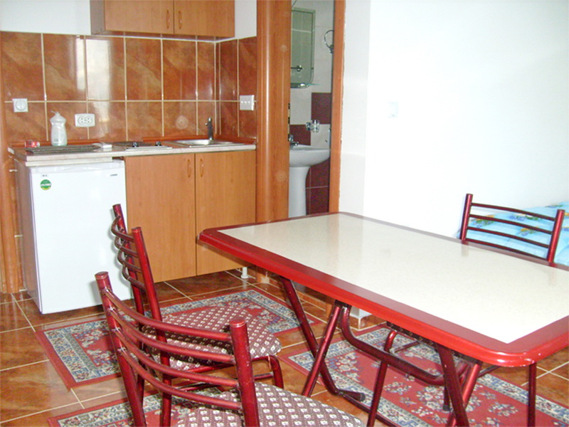 Küche mit Essbereich in einer Villa in Prčanj, Montenegro: Holzschränke, Fliesen, Tisch mit Stühlen und Blick auf das Badezimmer.