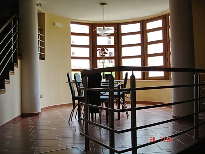 Living room with dining area and panoramic windows in a villa in Utjeha, Montenegro: tiled floor, columns, and staircase.