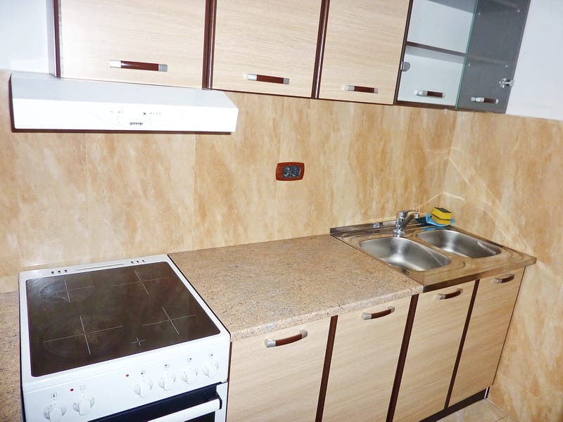 Küche in einer Wohnung in Rafailovići, Montenegro: helle Einbauküche, Elektroherd, Dunstabzugshaube und Edelstahlspüle.