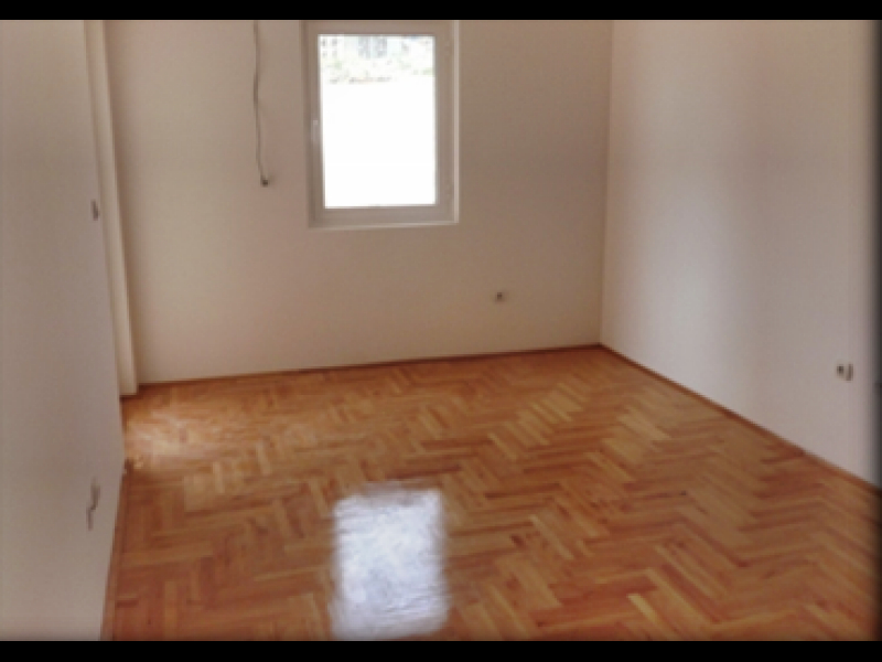 Salon lumineux et vide avec parquet et murs blancs dans un appartement à vendre à Igalo, Monténégro.