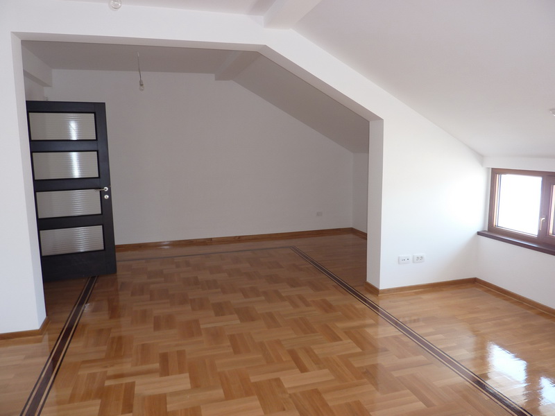 Helles Wohnzimmer in einer Dachgeschosswohnung in Budva, Montenegro: Parkettboden, weiße Wände und eine dunkle Innentür.