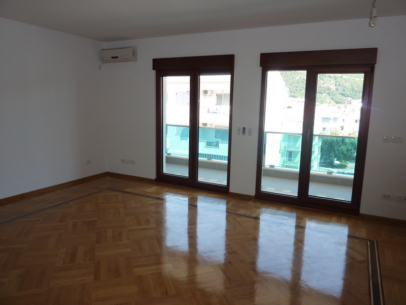 Helles Wohnzimmer mit Parkett und Zugang zum Balkon in einer Wohnung in Budva, Montenegro. Blick auf die Stadt und die Berge.