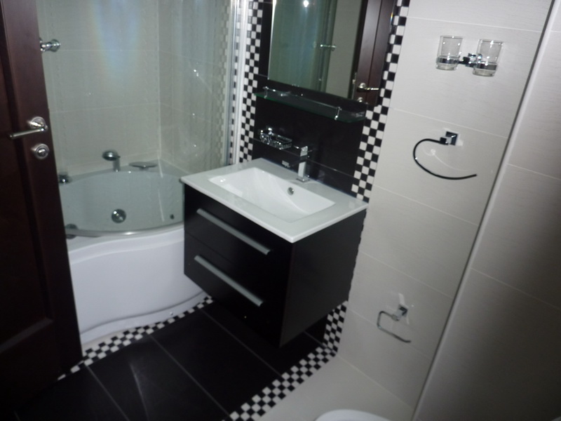Modernes Badezimmer in einer Wohnung in Budva, Montenegro: Eckbadewanne, stilvoller Waschtischunterschrank und dekorative Fliesen.