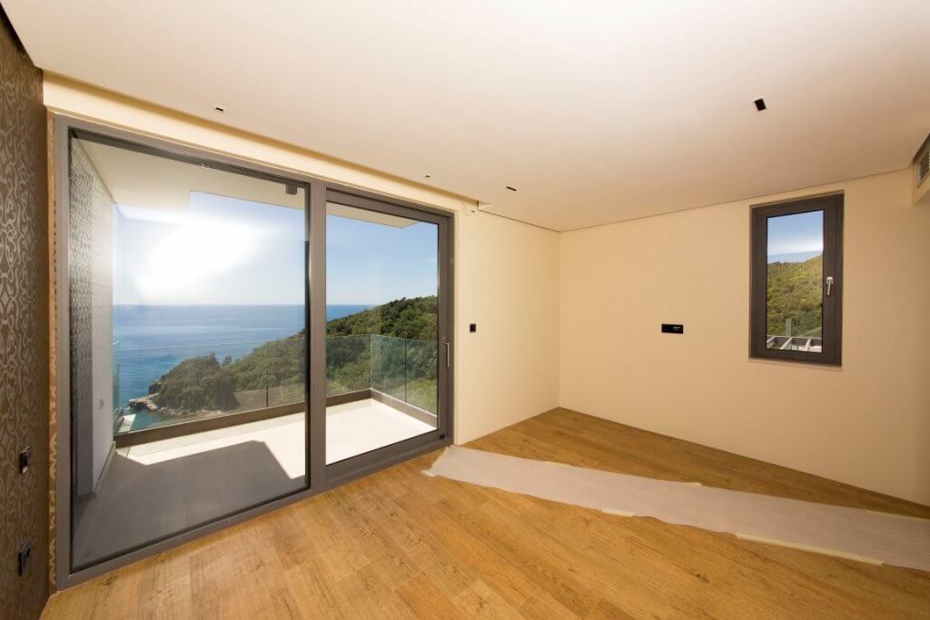 Schlafzimmer in einer Villa in Budva, Montenegro: Panoramafenster mit Meerblick, Terrasse und helle Innenausstattung.