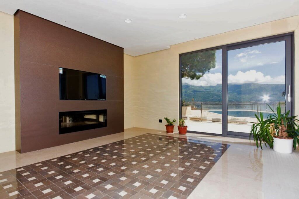 Wohnzimmer der Villa in Budva, Montenegro: Panoramafenster, Meerblick, moderner Kamin und stilvoller Fliesenboden.