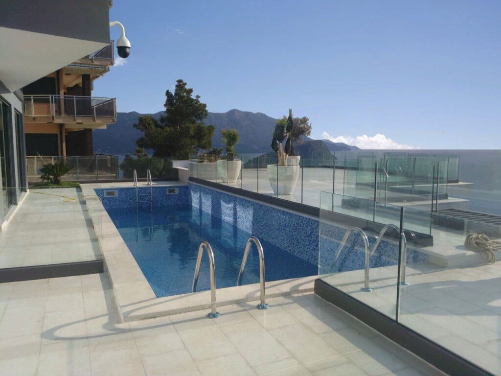 Offener Pool auf der Terrasse einer Villa in Budva, Montenegro, mit Panoramablick auf das Meer und die Berge, Glasgeländer.