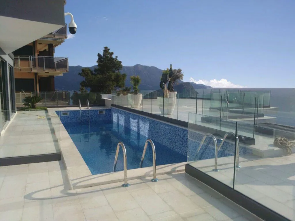 Offener Pool auf der Terrasse einer Villa in Budva, Montenegro, mit Panoramablick auf das Meer und die Berge, Glasgeländer.