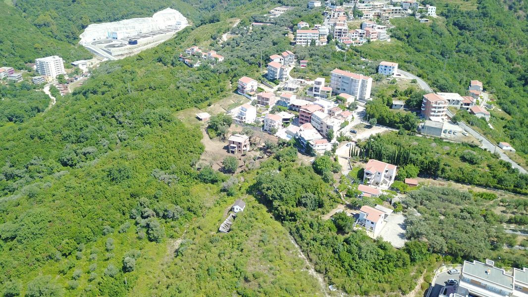 Luftaufnahme eines Grundstücks und einer Wohnbebauung in Bečići, Montenegro, zwischen Hügeln und dichtem Grün.