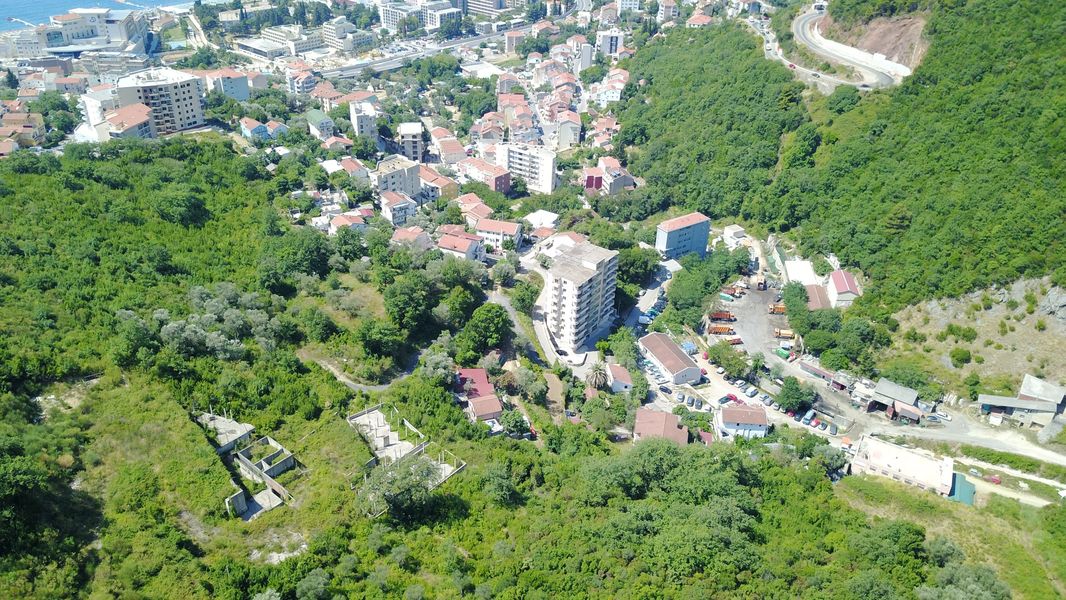 Luftaufnahme eines Grundstücks und einer Wohnbebauung in Bečići, Montenegro, mit Panorama auf Berge und Meer.