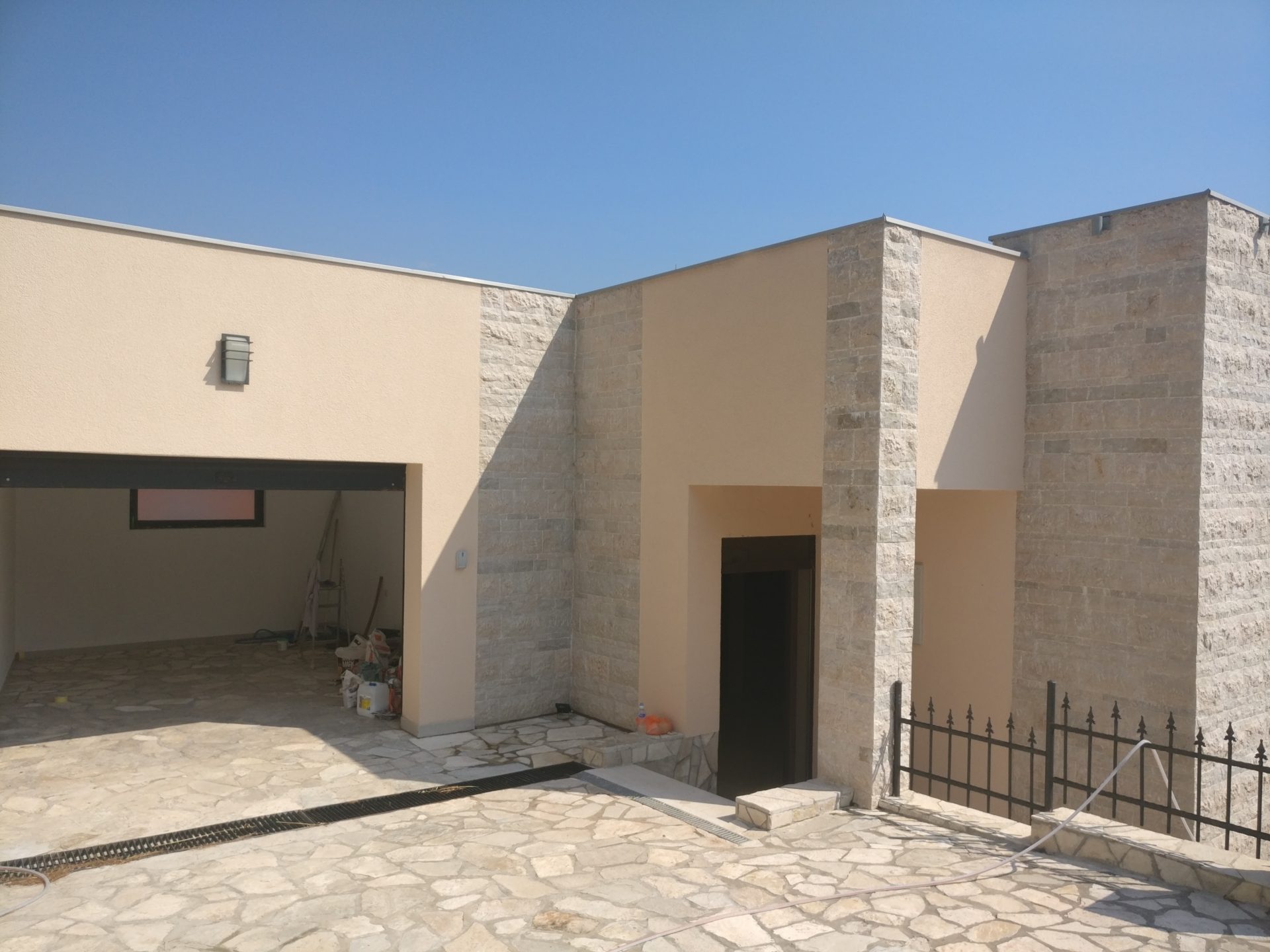 Modernes Haus in Šušanj, Montenegro: Fassade mit Steinverkleidung, Garage und mit Stein gepflasterter Vorbereich.