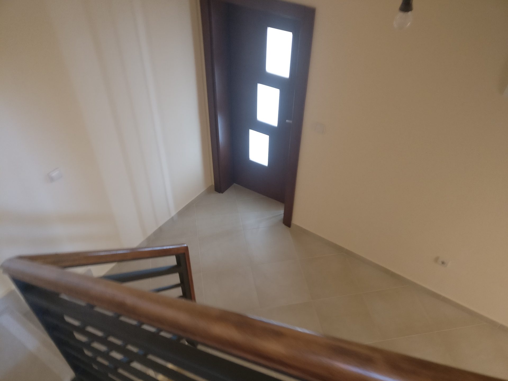 Blick von oben auf die Treppe mit Holzgeländer und die Eingangstür im Haus, Shushan, Montenegro. Helle Fliesen und Ausstattung.