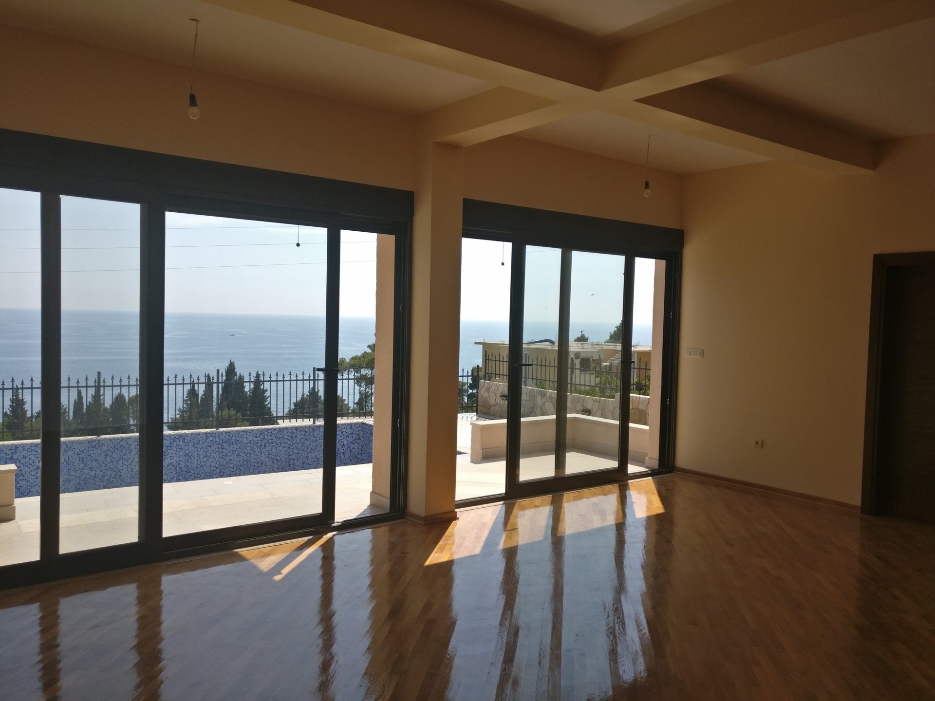 Wohnzimmer in einem Haus in Šušanj, Montenegro: Panoramafenster, Meerblick und Terrasse mit Pool, Parkettboden.