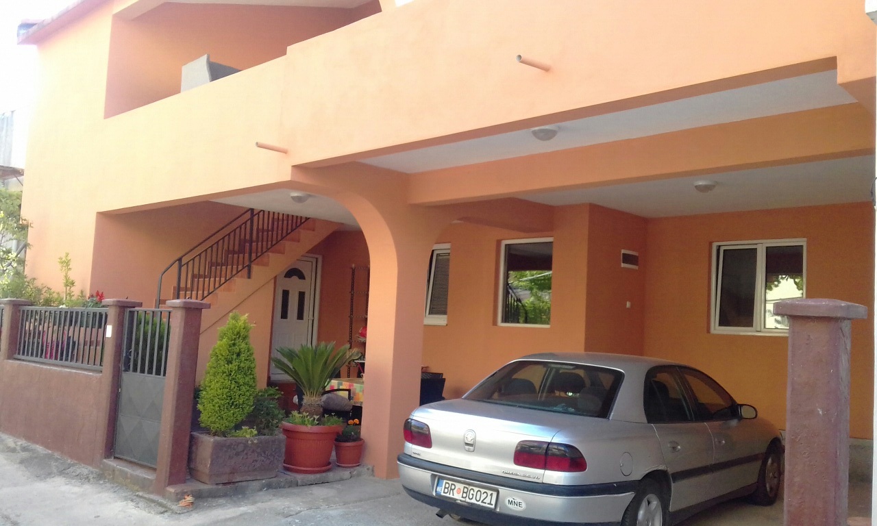 Zweistöckiges Haus in Šušanj, Montenegro: orangefarbene Fassade, überdachter Parkplatz und Außentreppe.