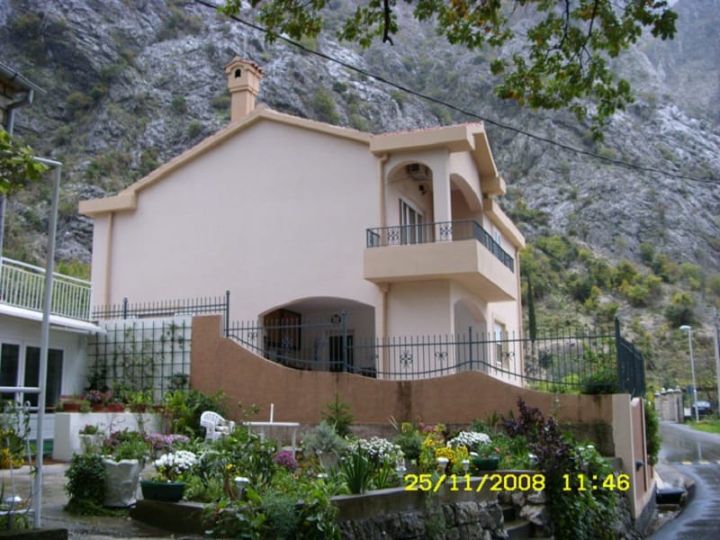 Maison à deux étages à Orahovac, Monténégro, avec balcon, terrasse et jardin bien entretenu sur fond de montagnes rocheuses.