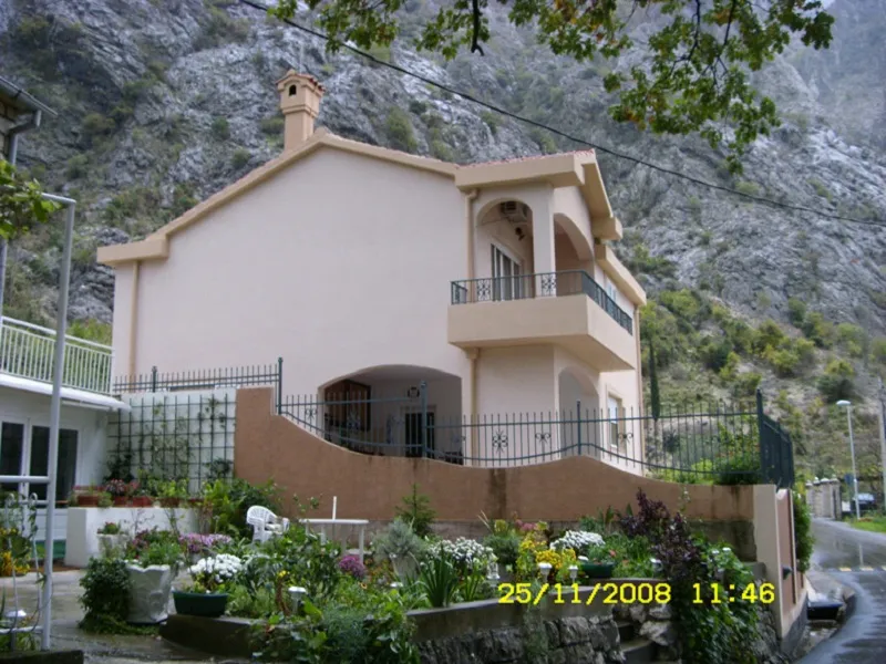Two-story house in Orahovac, Montenegro, with a balcony, terrace, and a well-kept garden against a backdrop of rocky mountains.