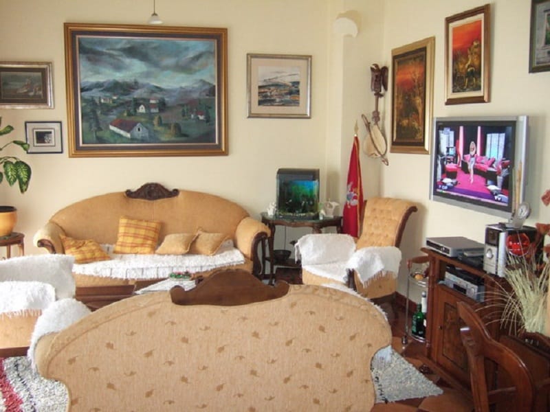 Salon confortable dans une maison à Orahovac, Monténégro : mobilier moelleux, tableaux aux murs, aquarium et coin TV dans l’intérieur.