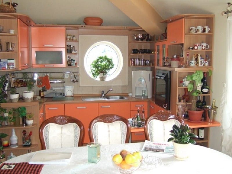 Cuisine chaleureuse avec un ensemble orange et une fenêtre ronde dans la maison, Orahovac, Monténégro. Coin repas avec des chaises classiques.