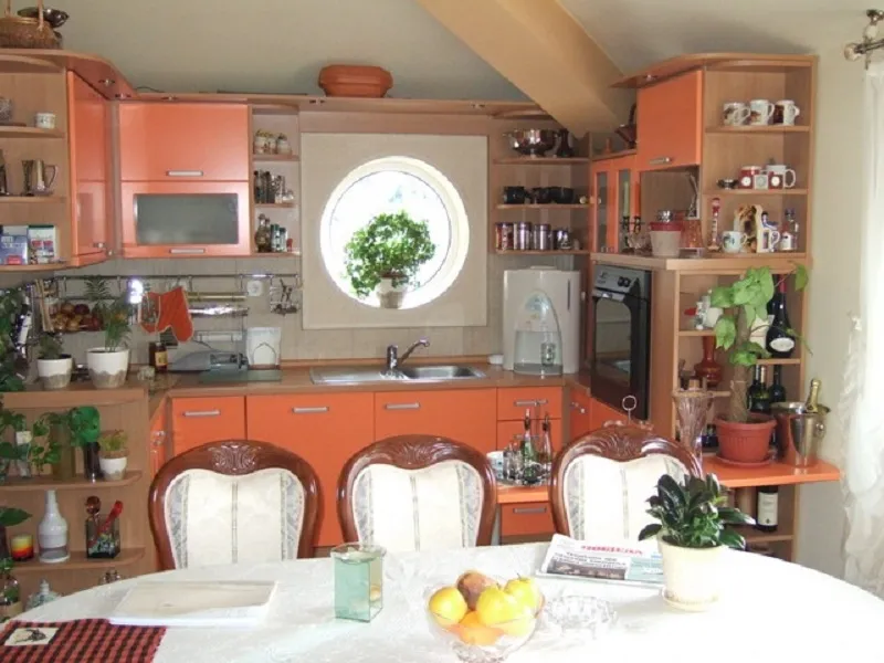 Cozy kitchen with an orange cabinet set and a round window in the house, Orahovac, Montenegro. Dining area with classic chairs.