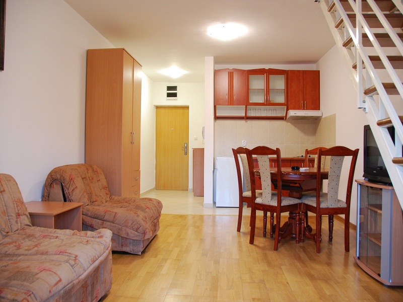 Wohnzimmer mit Sofa, Küchenbereich, Esstisch und Treppe zum Obergeschoss.