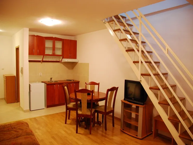 Wohnzimmer mit kleiner Küche, Essbereich, Fernseher und Holztreppe.